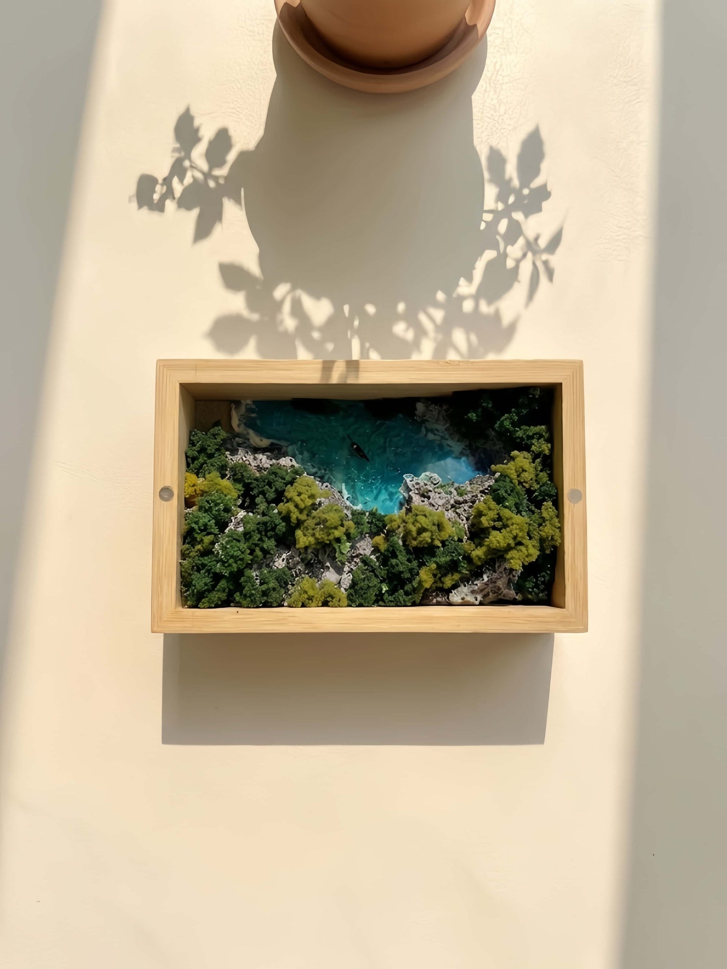 Framed picture of a coastal landscape with trees and water on a light background