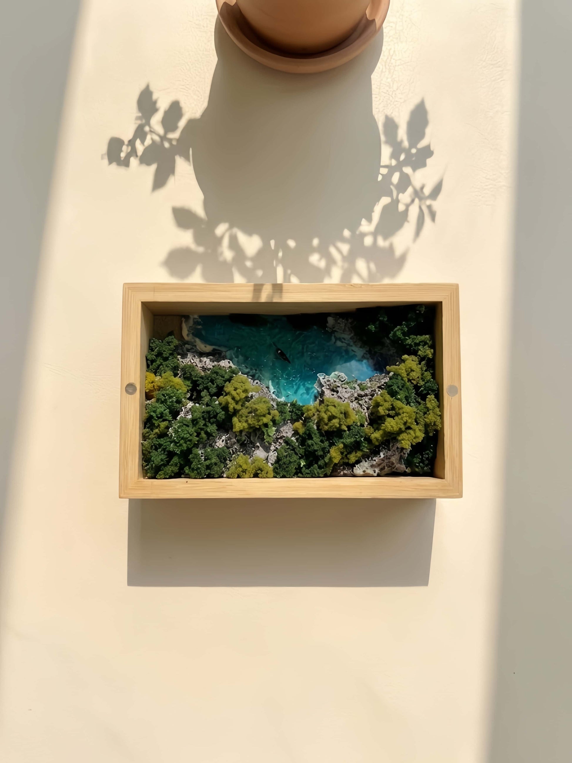 Framed picture of a coastal landscape with trees and water on a light background