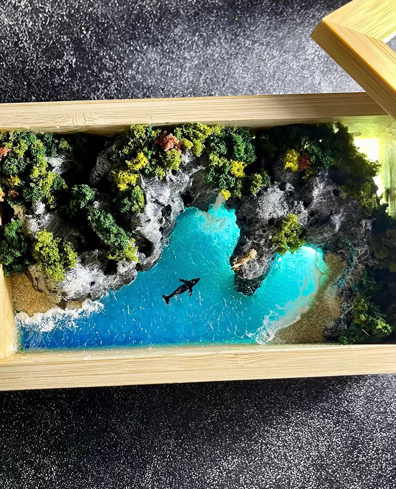 Model of a coastal scene with a shark in the water, framed by a wooden border.