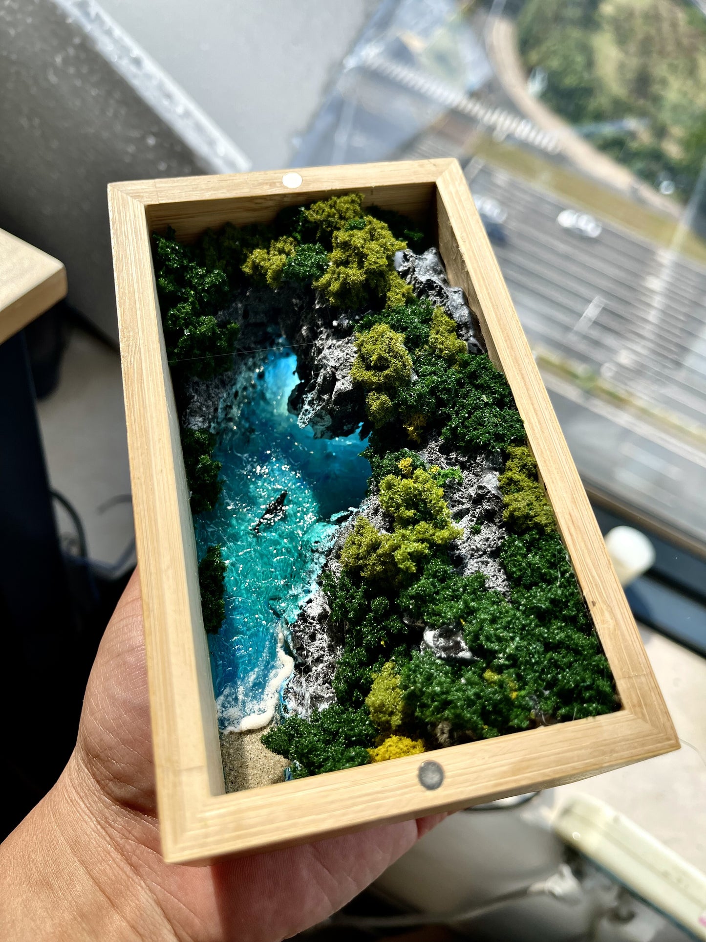 Wooden box with a scenic view of a river and trees held by a hand.